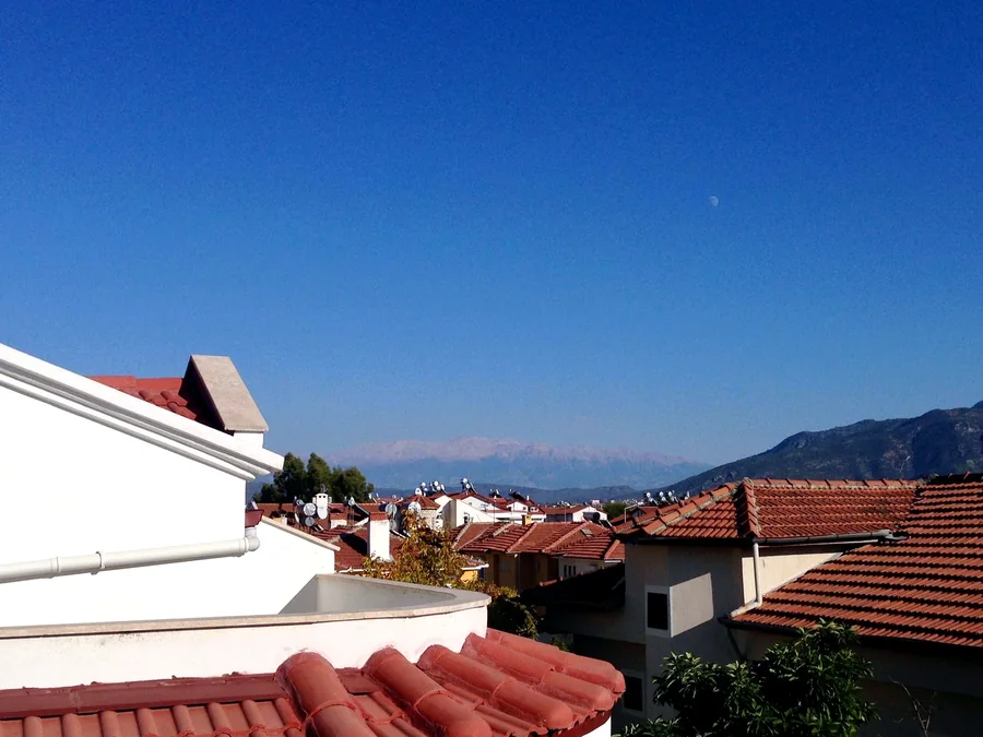 Balcony view towards rooftops, mountains and sea near Çalış Fethiye